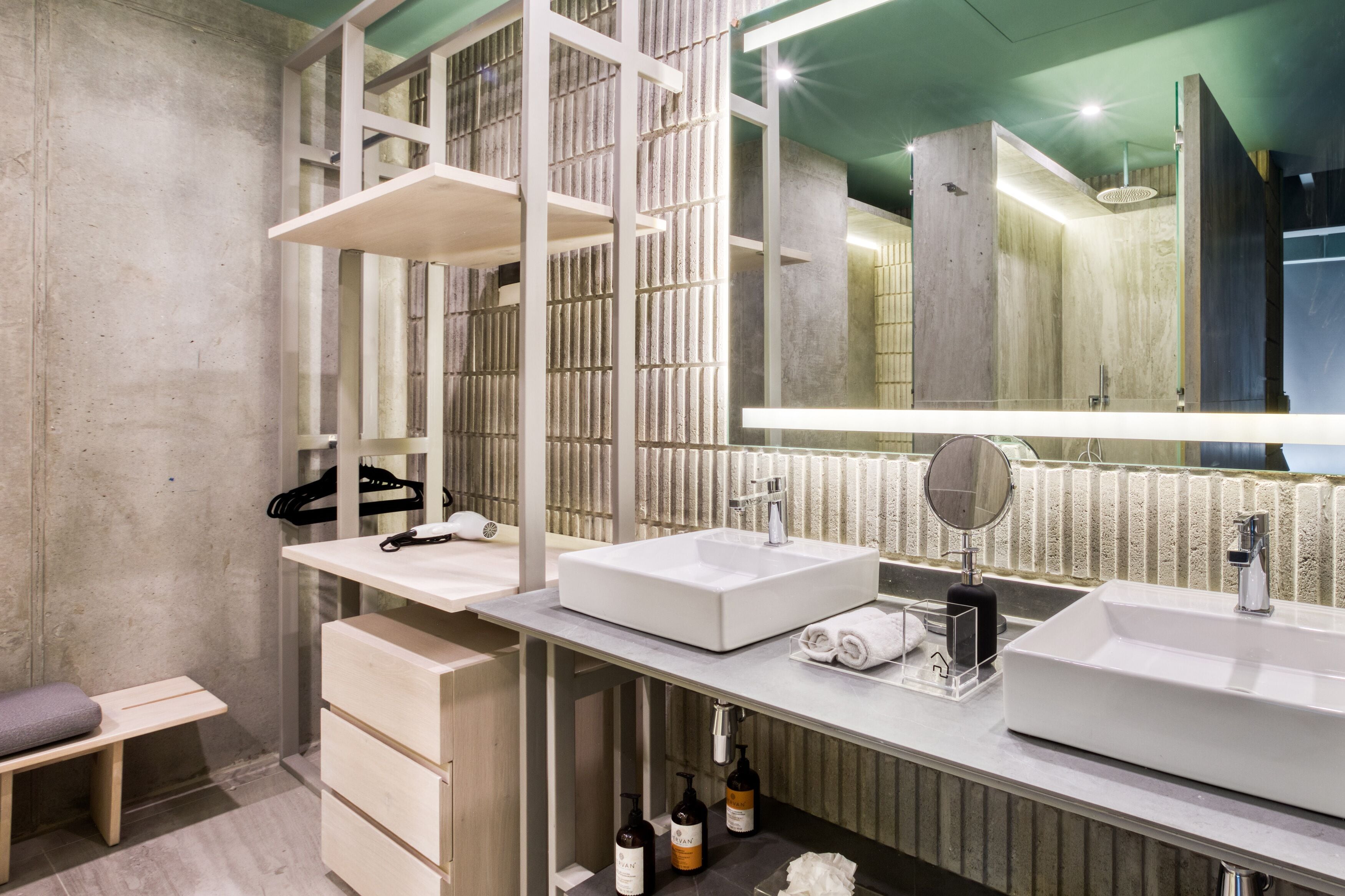 A modern bathroom with two sinks, a bench, and a large mirror.