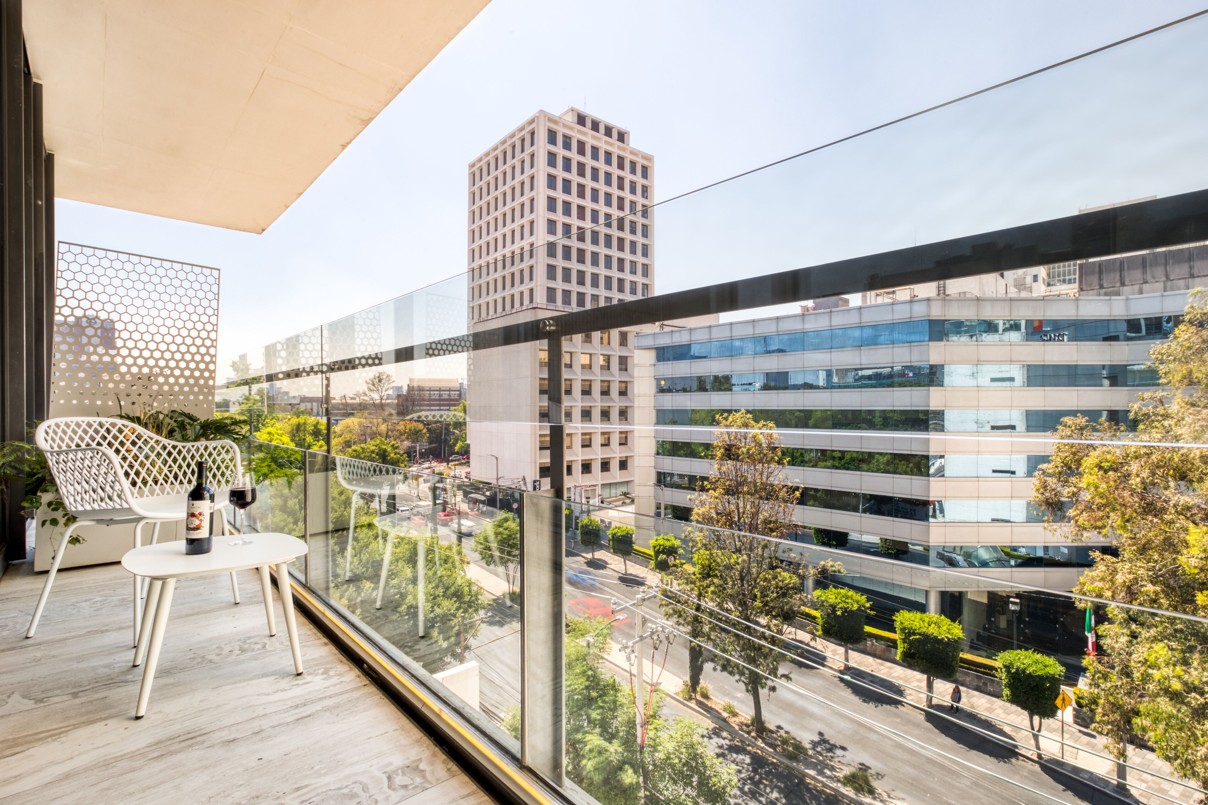A balcony with a table and chairs, overlooking a cityscape with modern buildings and a clear sky.