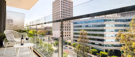 A balcony with a table and chairs, overlooking a cityscape with modern buildings and a clear sky.