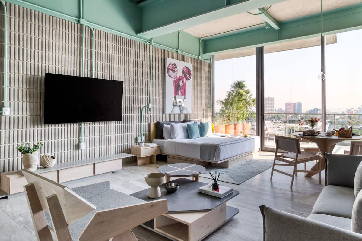 A modern living room with a large flat-screen TV, a sofa, a dining table, and a balcony with a city view.