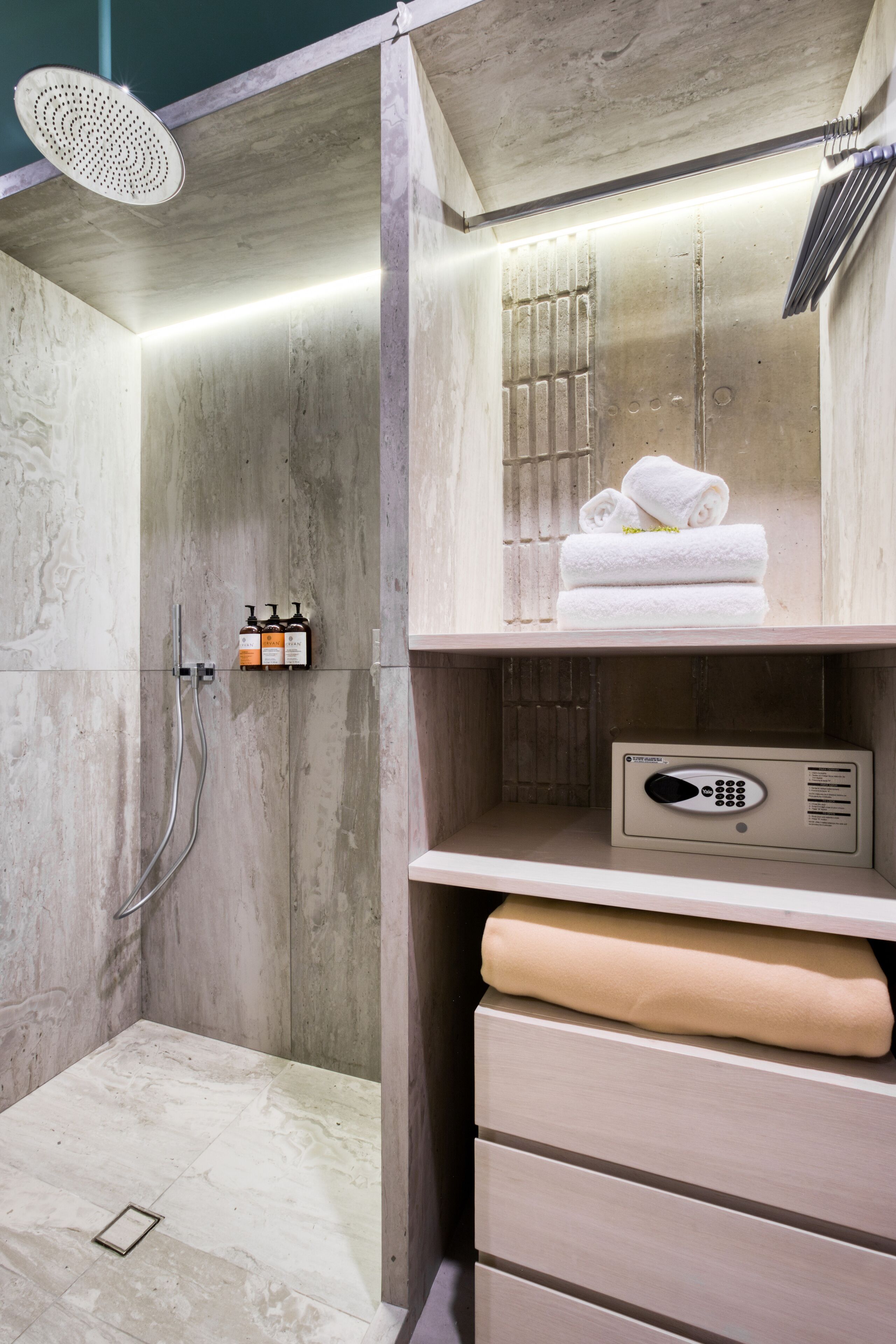 Un espace douche moderne doté d’un pommeau de douche à main, d’un panneau de commande et de serviettes soigneusement pliées, rangées sur une étagère.