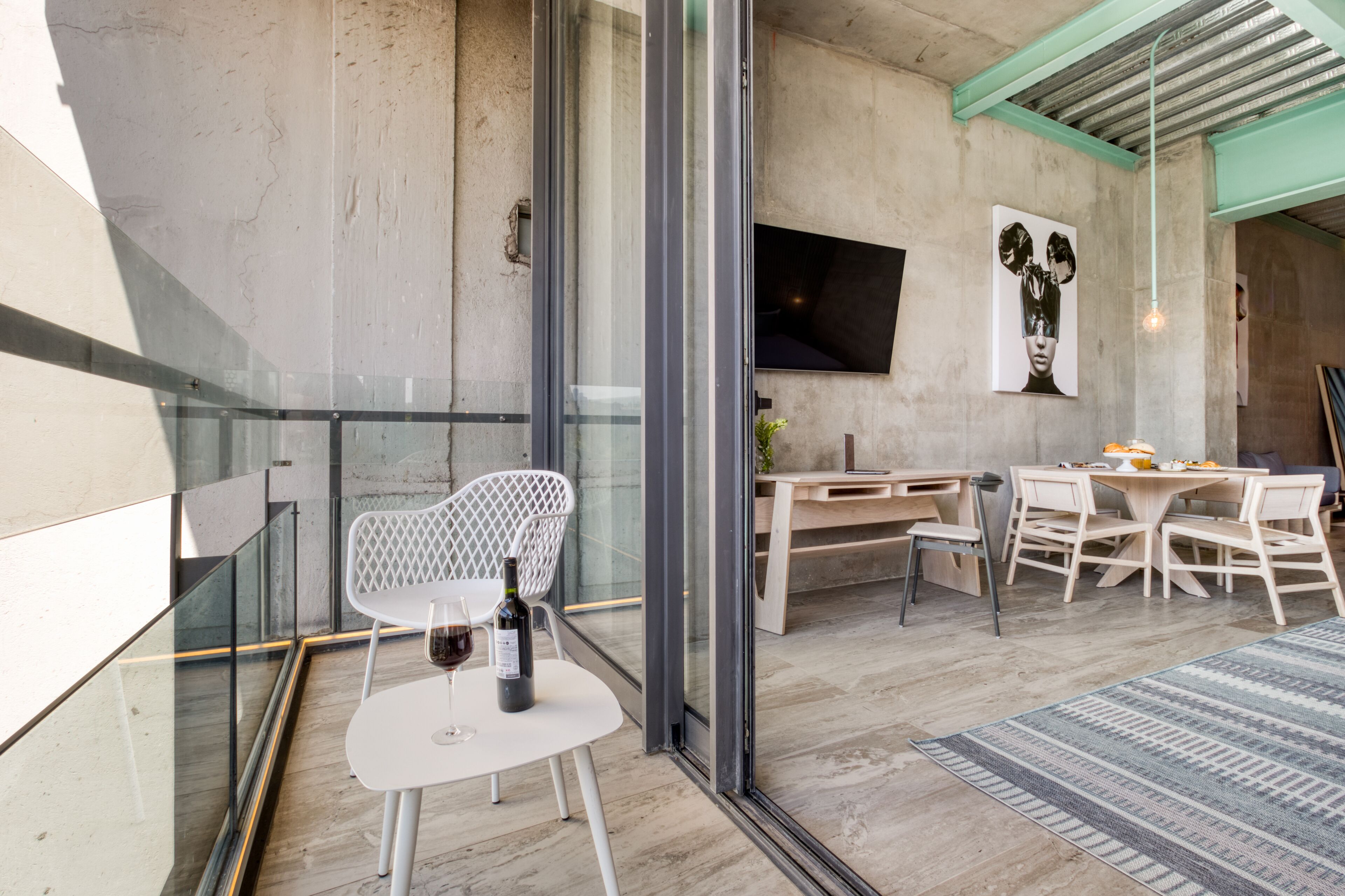 Un interior moderno con barandilla de vidrio, una silla blanca, una mesa de comedor con sillas y un televisor de pantalla plana montado en la pared.