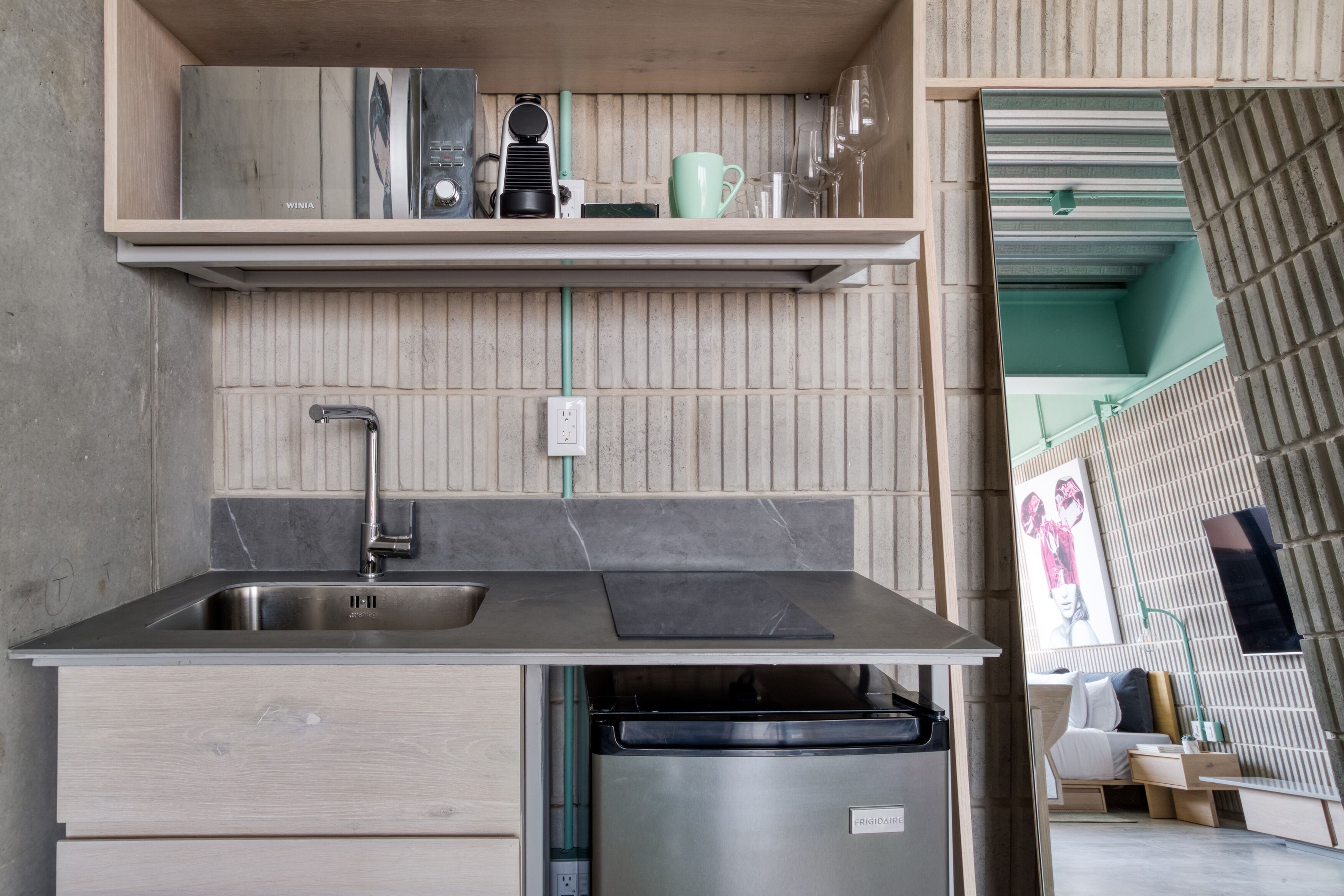 A compact kitchen with a sink, dishwasher, and a countertop with a coffee maker and a mug.