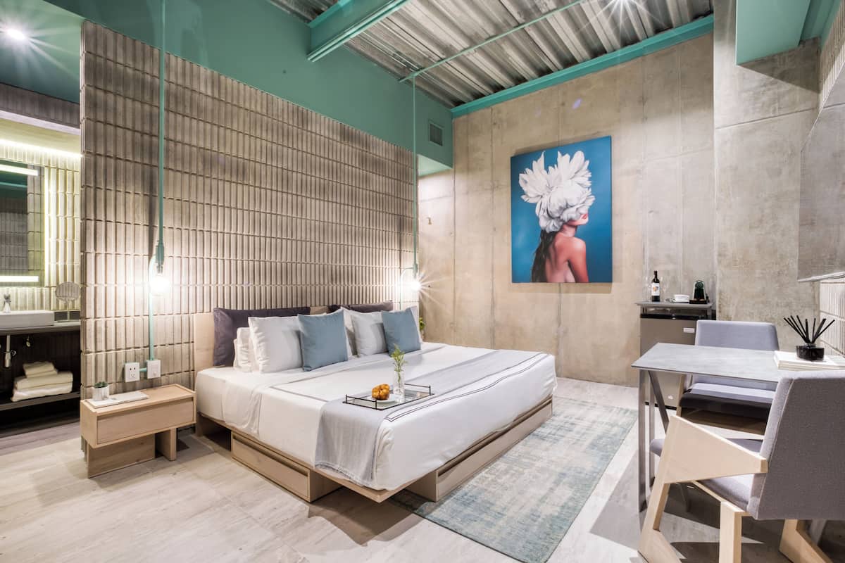 A modern bedroom with a large bed, bedside tables, a desk, and a painting on the wall.