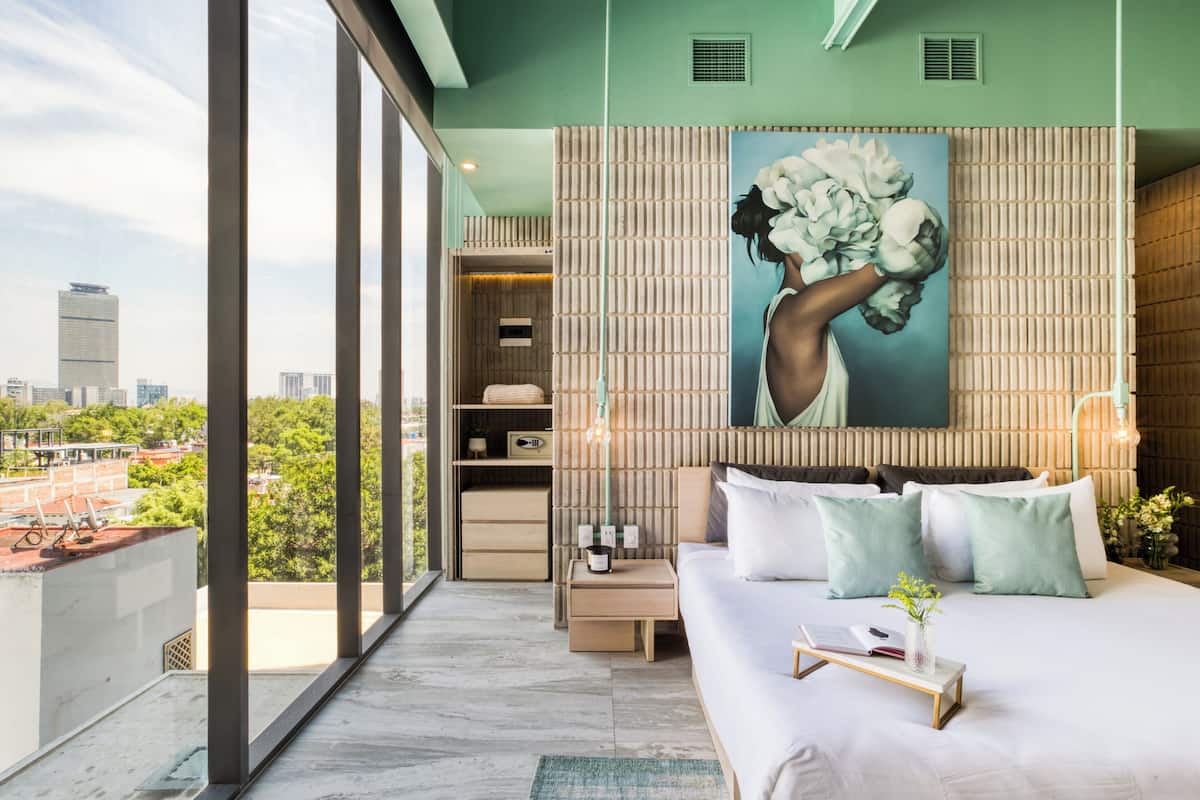 A modern hotel room with a large bed, a city view, a wooden accent wall, and a large painting.