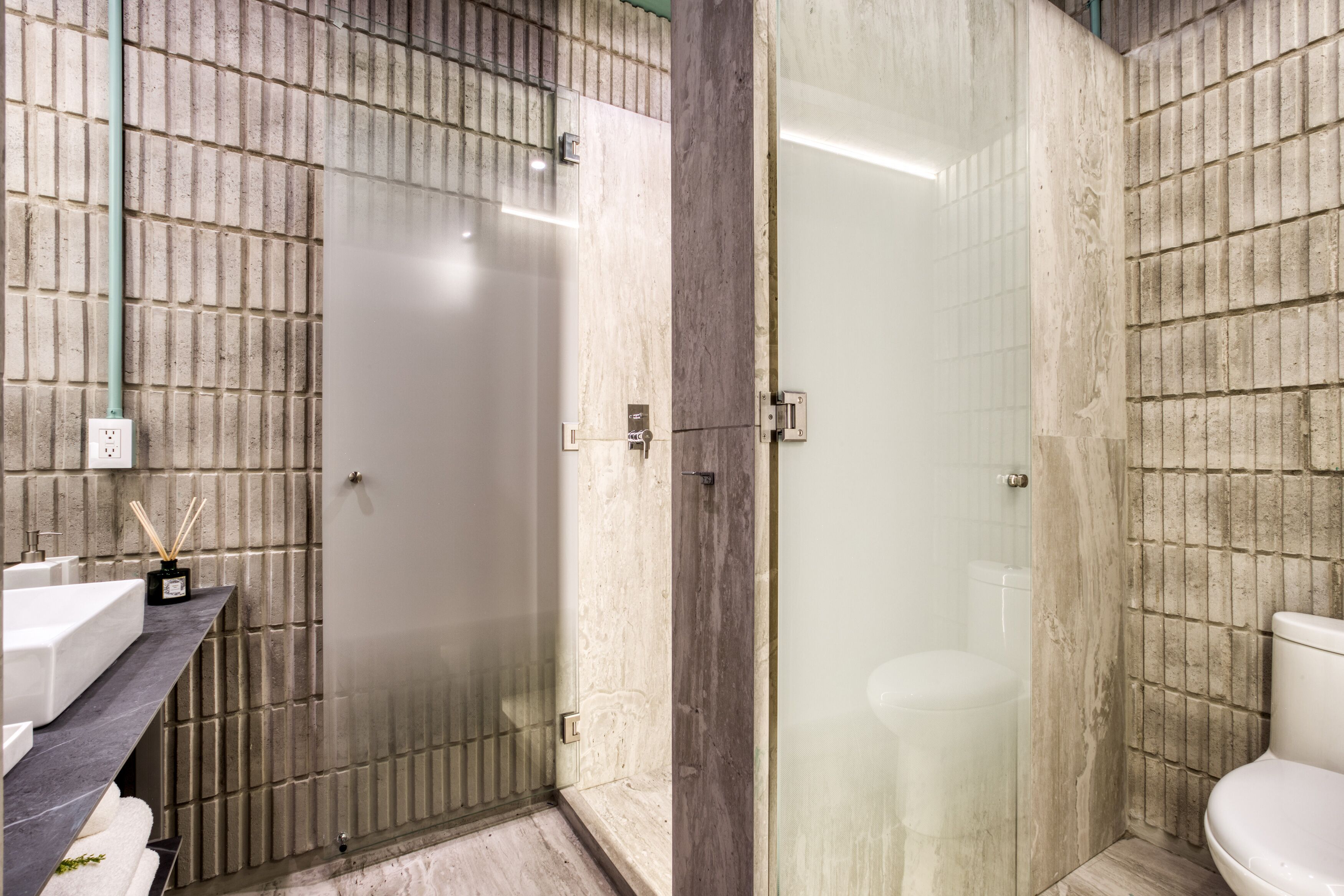 Ein Badezimmer mit gefliesten Wänden, einer Glasdusche, einem weißen Waschbecken und einer Toilette.
