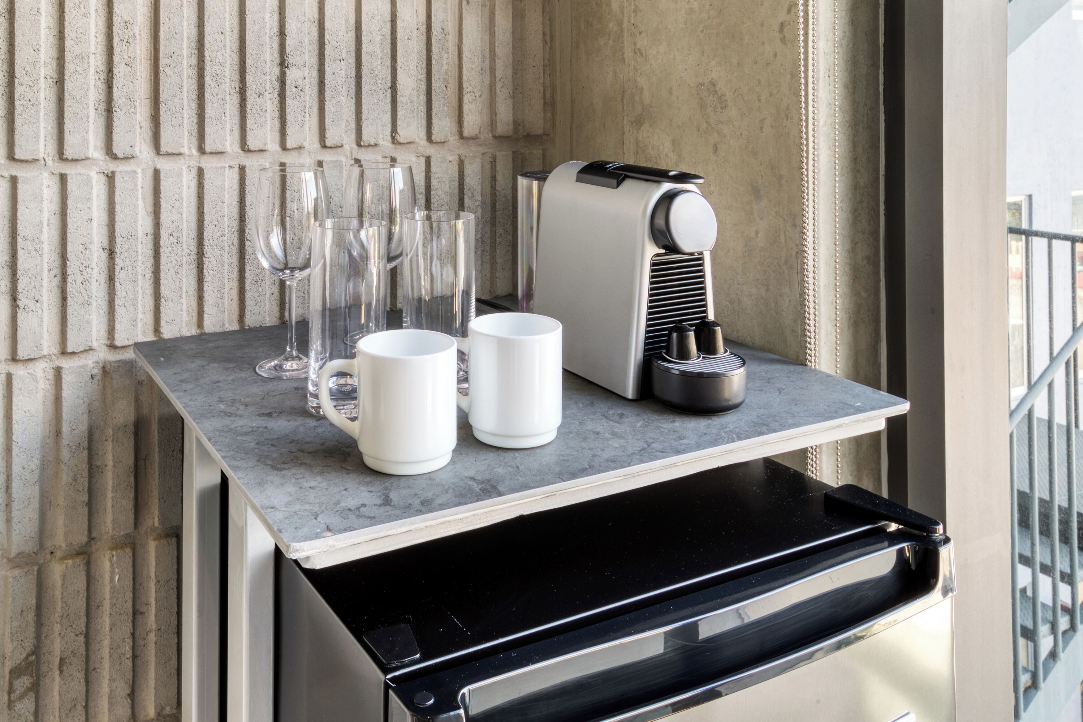 Una cafetera, dos tazas blancas y varios vasos sobre una encimera.