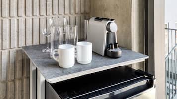 A coffee machine, two white mugs, and several glasses on a countertop.