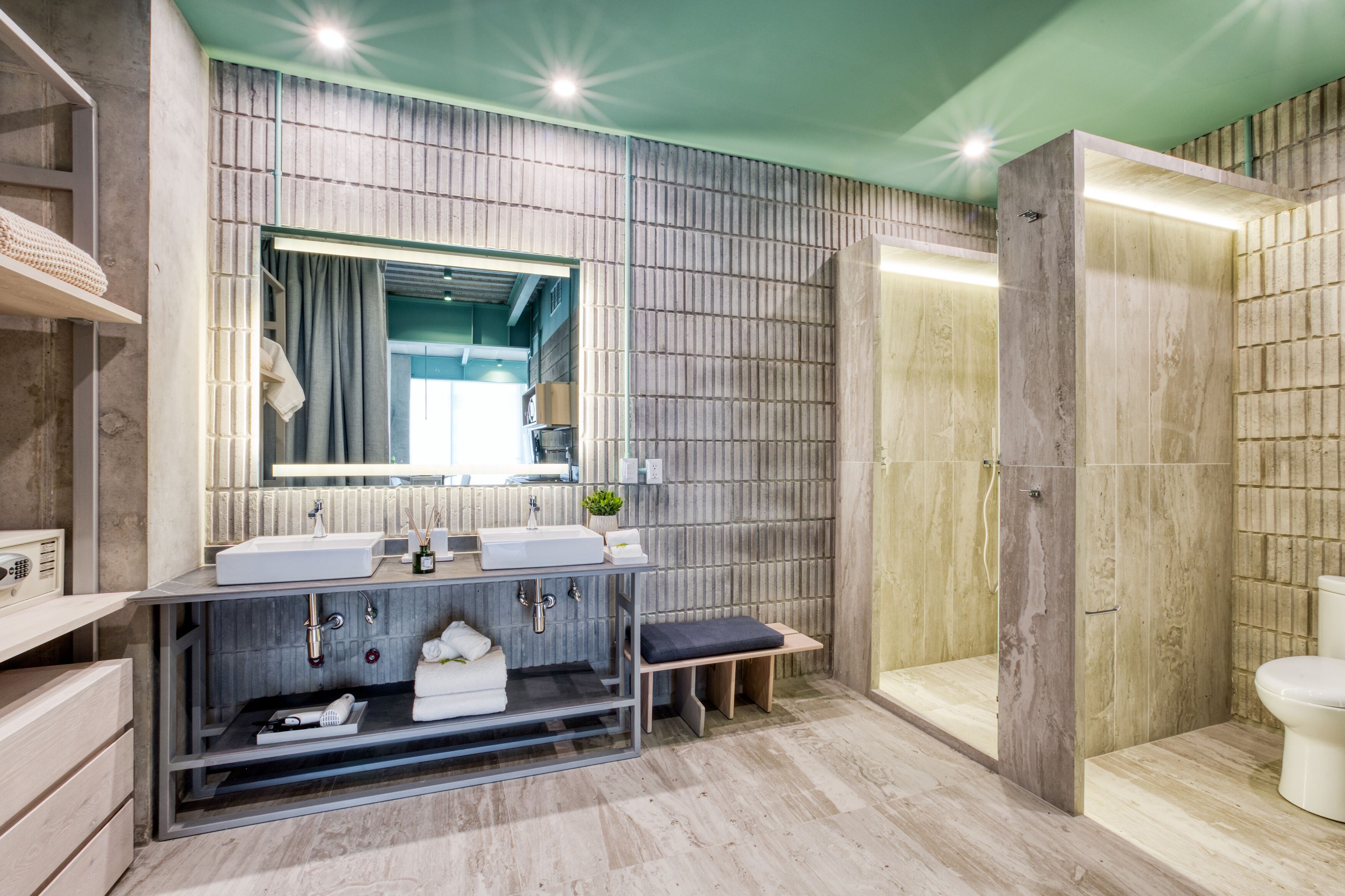 Un baño moderno con un espejo grande, dos lavamanos, un banco y una zona de ducha.