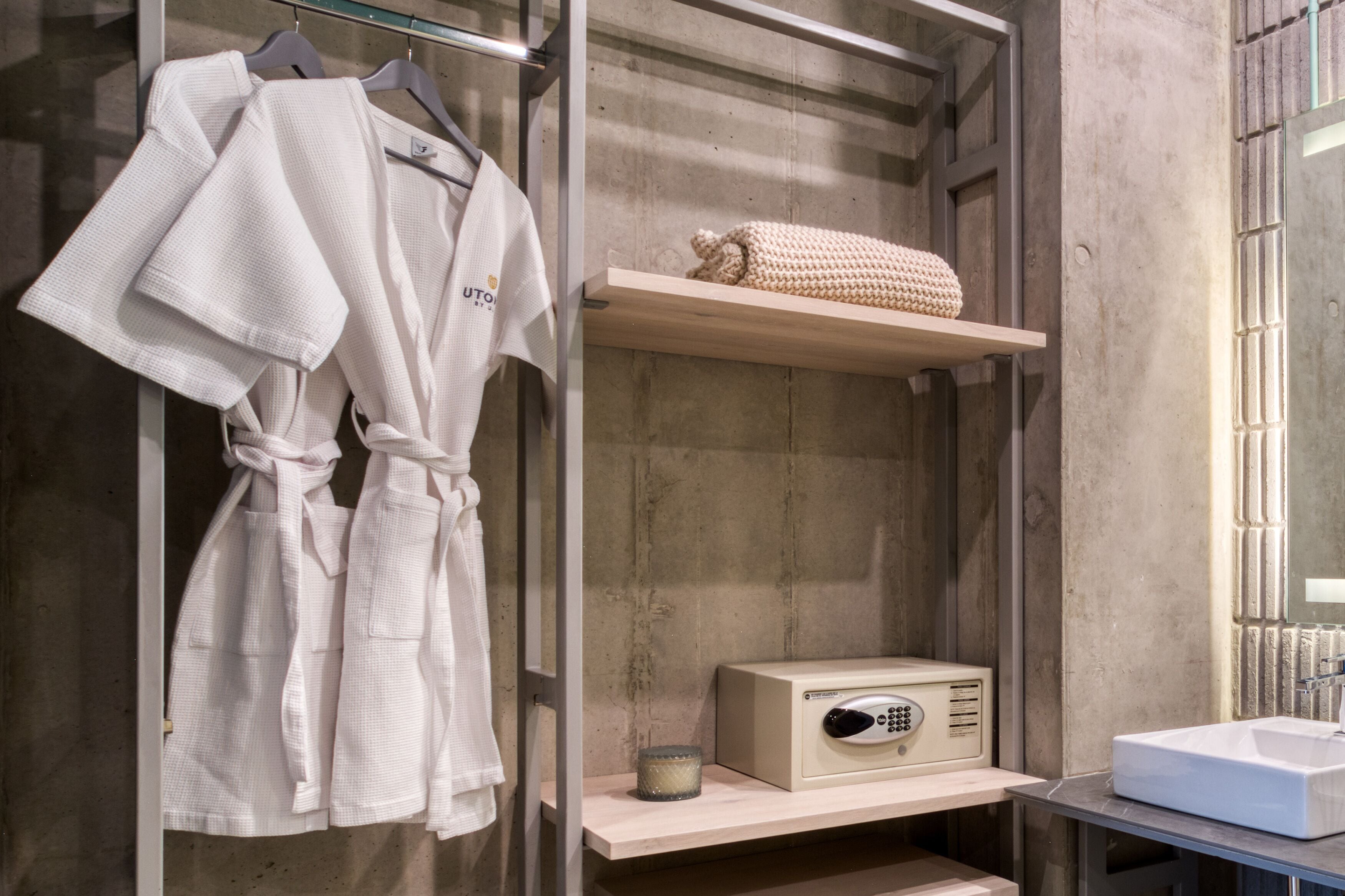 A bathroom with a wooden vanity, a towel rack with white robes, a small shelf with a knitted item, and a radio.