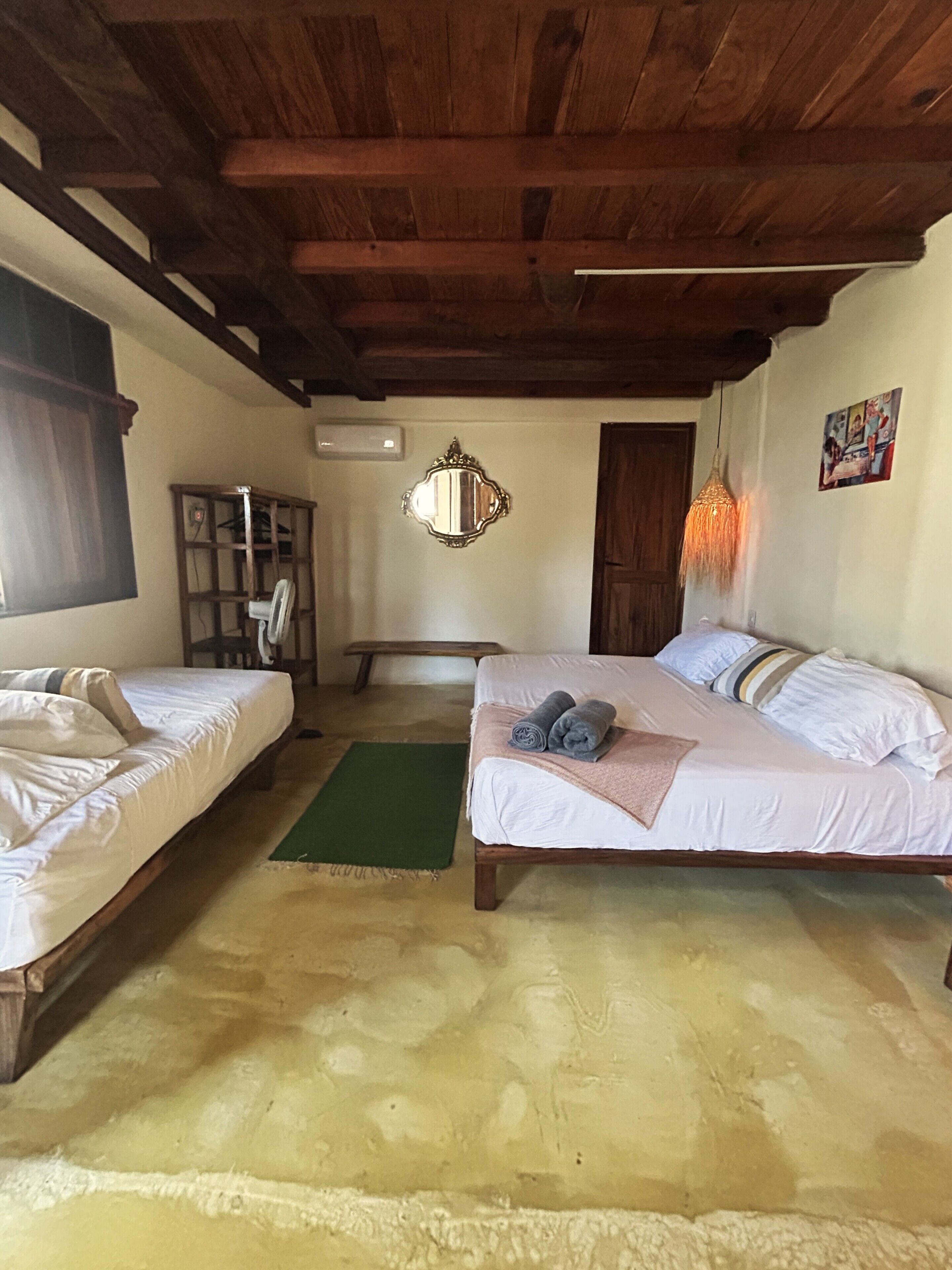 Una habitación con dos camas, un banco, un espejo y una lámpara colgante.