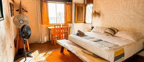 Un dormitorio rústico con una cama de madera, un banco, un ventilador y vistas al exterior.