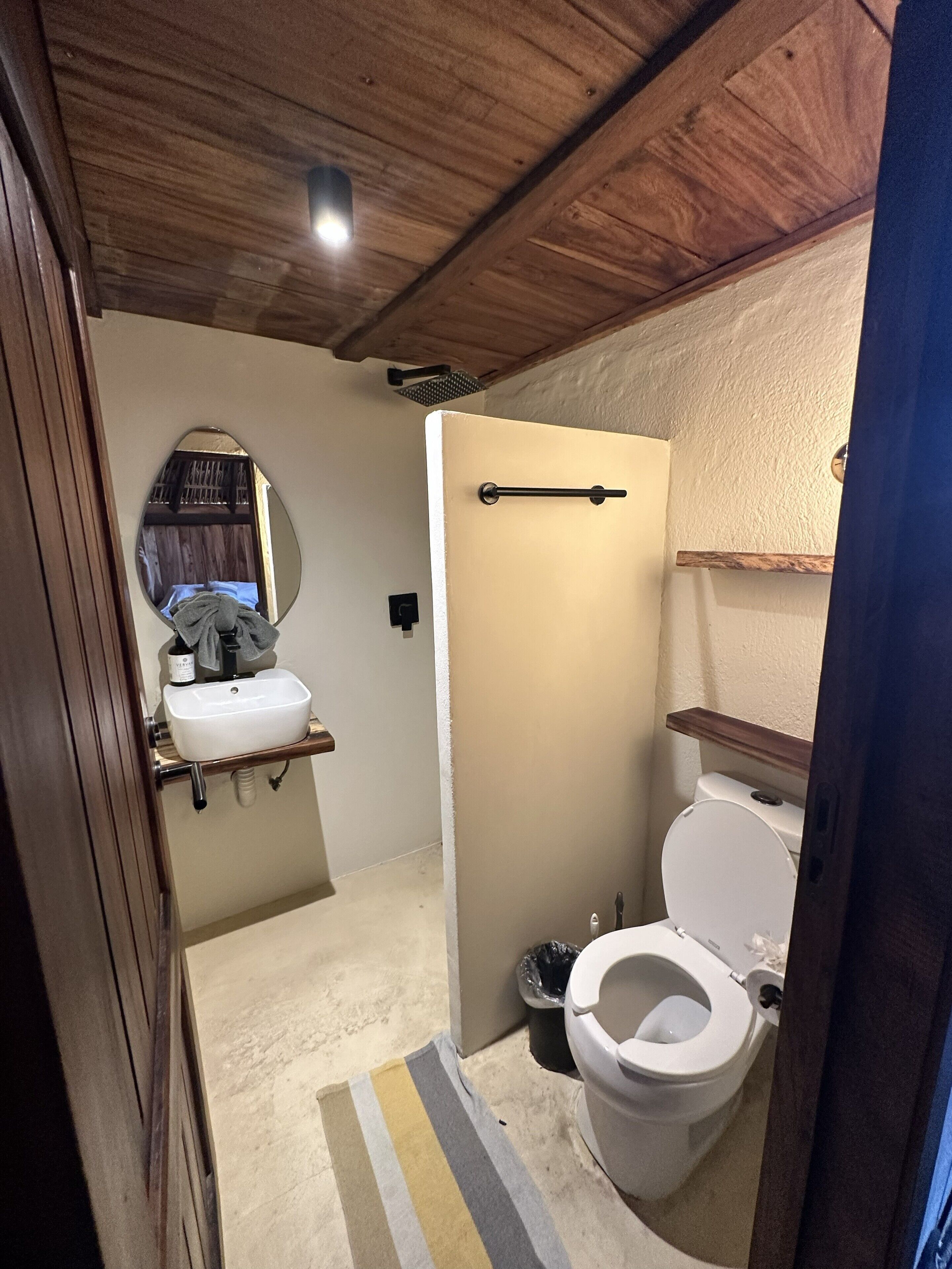 Un baño pequeño con inodoro blanco, lavamanos con espejo y zona de ducha.