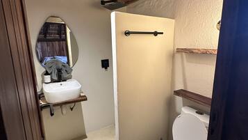 Un baño pequeño con inodoro blanco, lavamanos con espejo y zona de ducha.