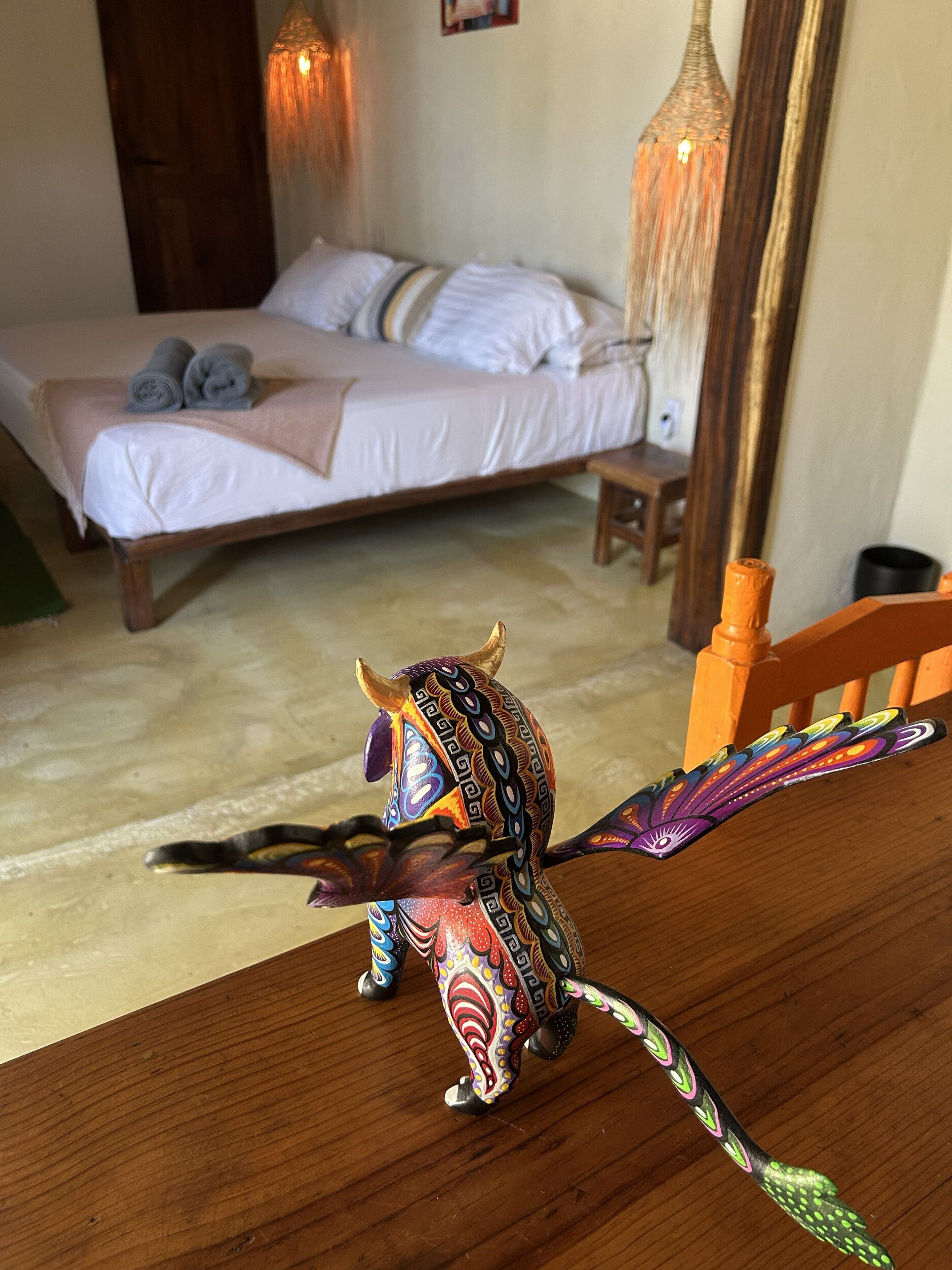 Una habitación con una cama, una silla de madera y una figurita de animal de colores.