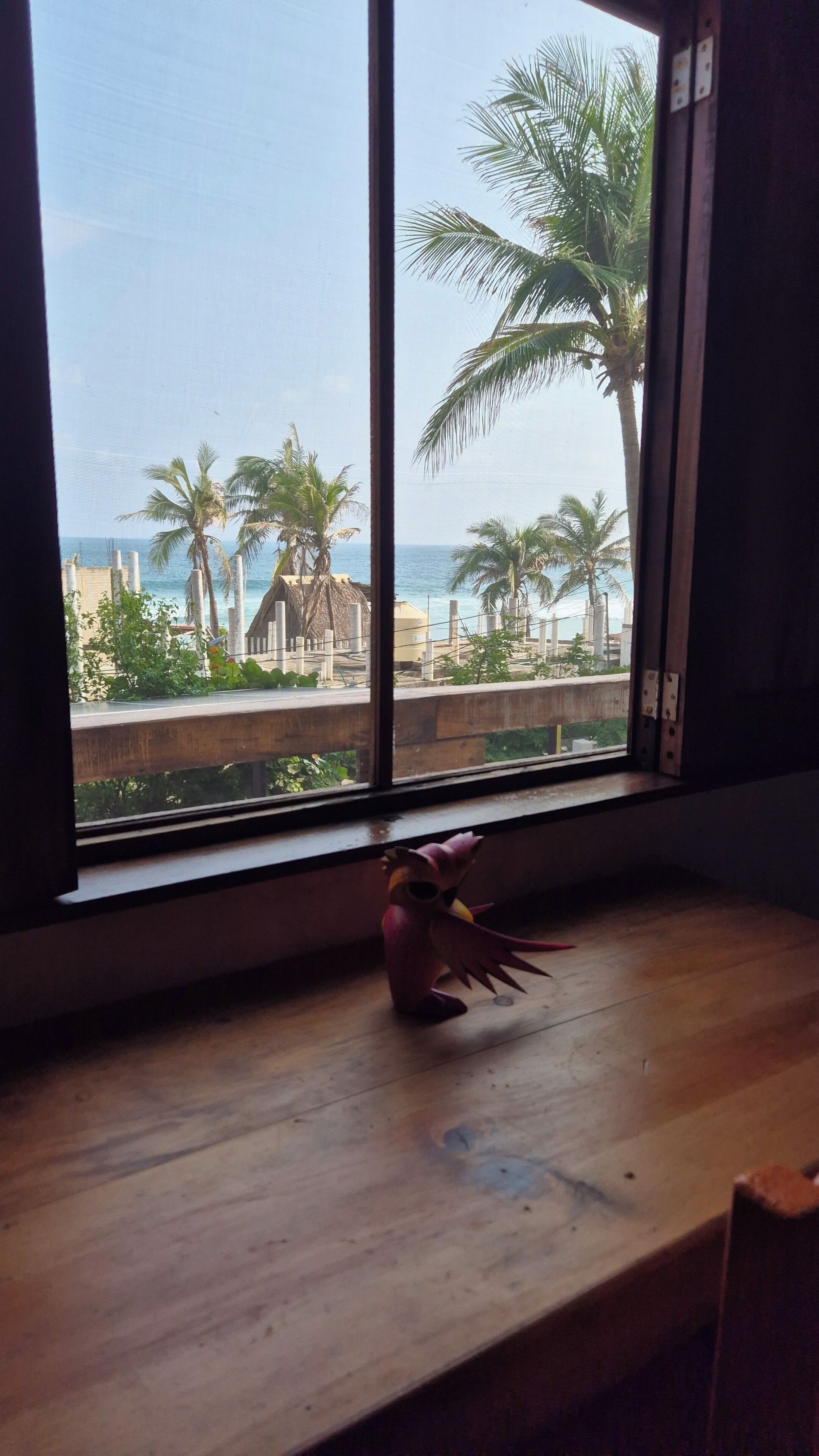 Una ventana con vista a una playa, palmeras y un edificio al fondo.