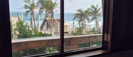 Una ventana con vista a una playa, palmeras y un edificio al fondo.