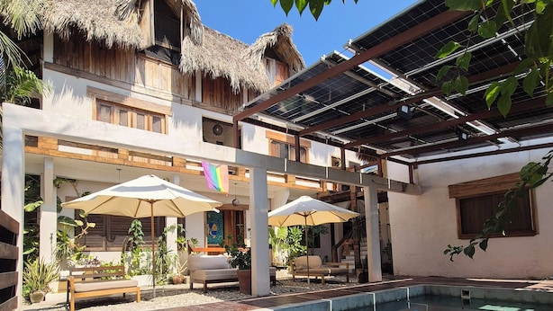 A pool area with lounge chairs and umbrellas, a thatched-roof structure, and a covered seating area. - Casa Playa del Amor (San Pedro Pochutla)