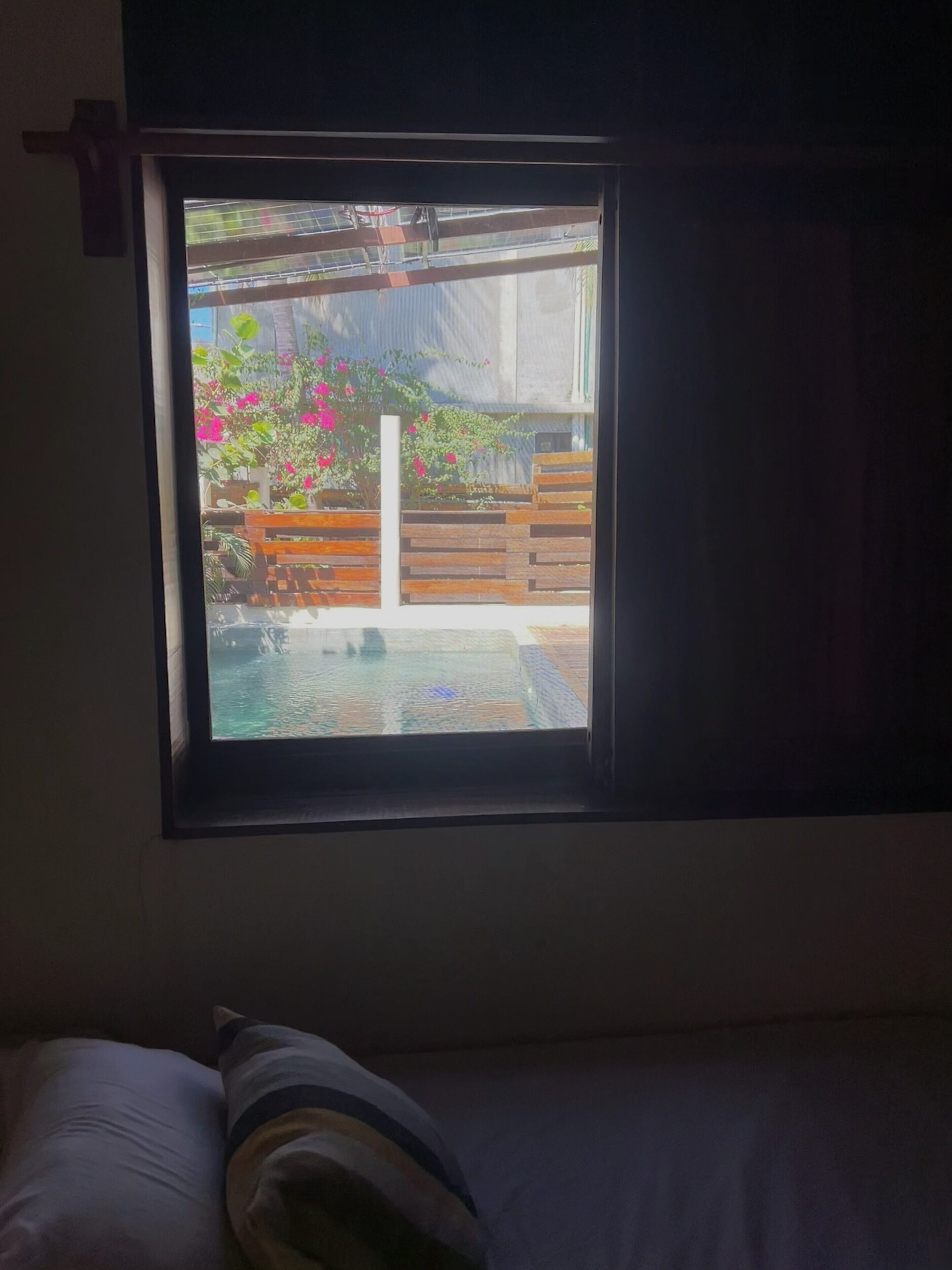 Quarto com janela dando para um jardim com cerca de madeira e uma piscina pequena.