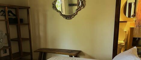 A room with a bed, a wooden bench, a mirror, and a wall-mounted air conditioner.
