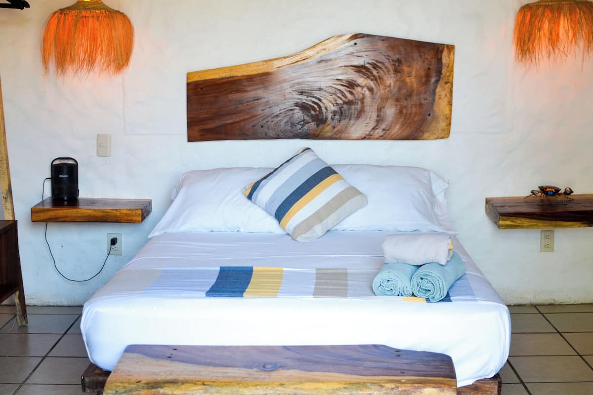 A neatly made bed with a striped pillow, a rolled towel, and a wooden headboard. There are two bedside tables with a lamp on each.
