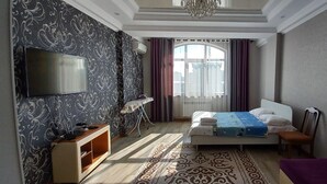A bedroom with a bed, a TV, a desk, and a window with curtains.