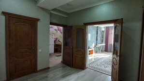 A hallway with wooden doors, a patterned rug, and a glimpse of a bathroom with a shower and a towel rack.