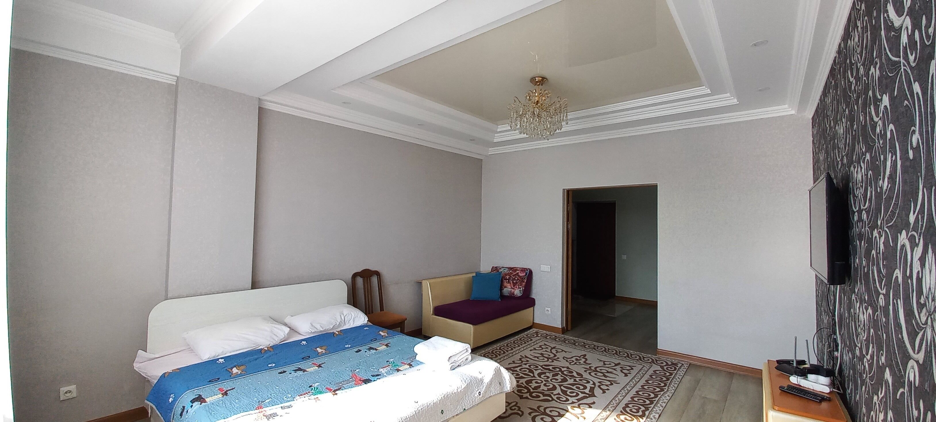 Un dormitorio con cama, una silla, un televisor y un tapete estampado.