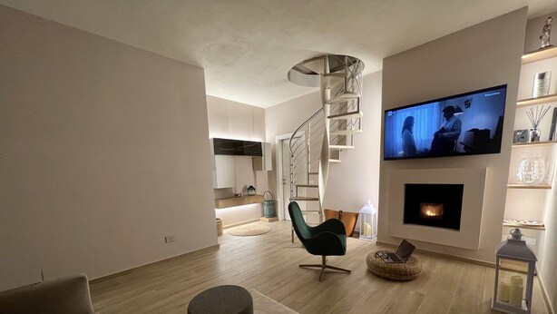 A modern living room with a flat-screen TV, a fireplace, a spiral staircase, and a cozy seating area. - MODERN DESIGN VILLA OVERLOOKING THE GULF OF MARINA DI CAMPO (Campo nell'Elba)