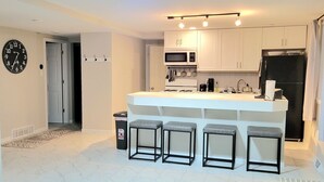 A modern kitchen with white cabinets, a black refrigerator, and a bar area with stools. - Modern Retreat on Lake Superior, close to the Snowmobile trails! (Baraga)