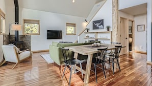 Ein geräumiges Wohnzimmer mit Holzesstisch, grünem Sofa und einem Steinkamin.