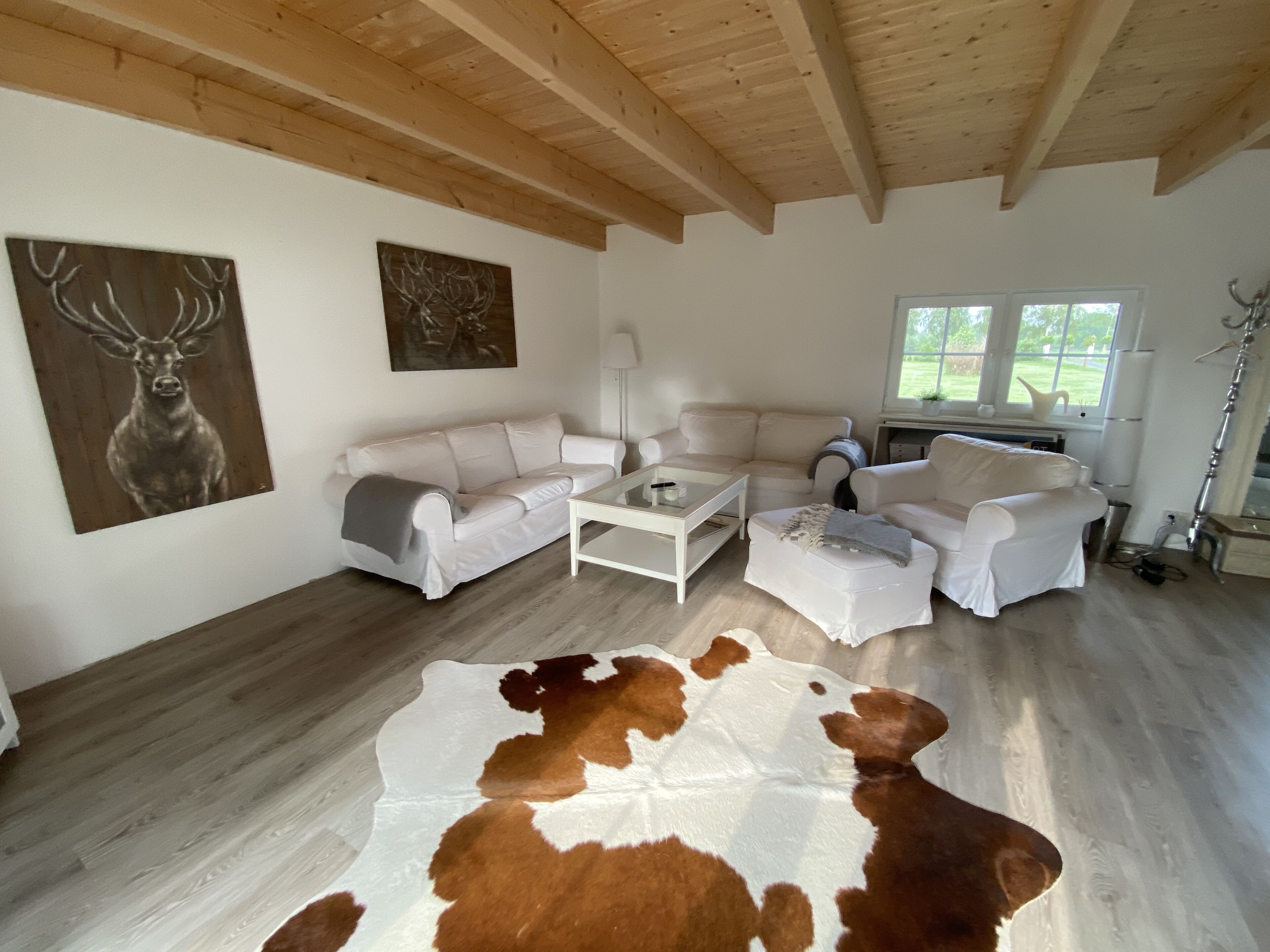 A spacious living room with a white leather sofa, a glass coffee table, and a cowhide rug.
