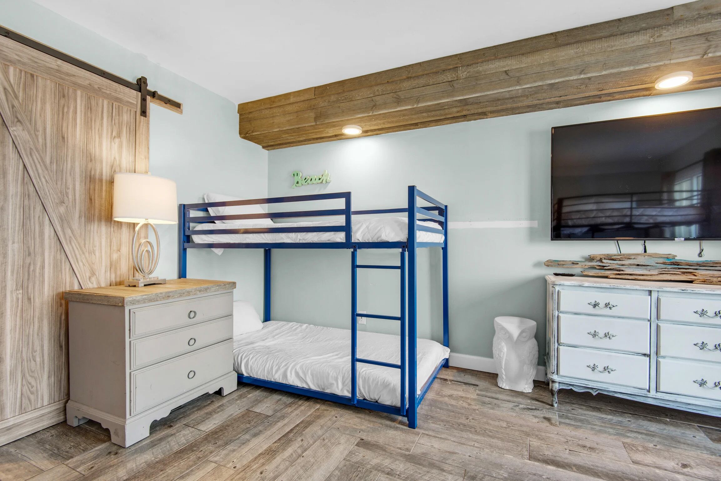 A bunk bed with a ladder, a dresser, a lamp, and a wall-mounted TV.