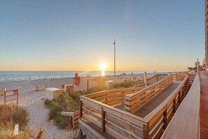 Una pasarela de madera que conduce a una playa, con un atardecer de fondo.