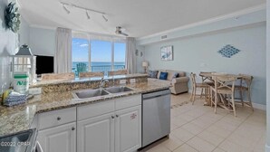 A kitchen with a view of the ocean, a dining area with a table and chairs, and a living room with a sofa and a TV. - Super clean, lower level, recently renovated and beachfront - walk to Pier Park (Panama City Beach)