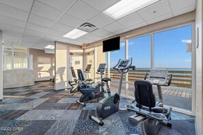 A fitness center with cardio machines, a television, and a view of the beach.
