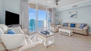 A spacious living room with a large TV, a sofa, a coffee table, and a balcony with a view. - Super clean, lower level, recently renovated and beachfront - walk to Pier Park (Panama City Beach)