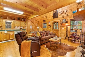 A cozy cabin interior with wooden walls, a leather sofa, a dining table, and a rustic decor. - Finding Bigfoot (2-Bedroom Home) by RedAwning (Sevierville)