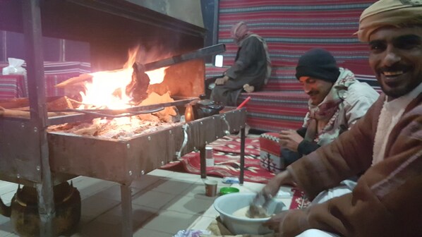 A traditional cooking setup with a fire, cooking utensils, and a person preparing food. - Wadi Rum Oasis (Wadi Rum)