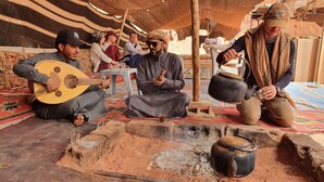 A group of people sitting on a colorful carpeted floor in a tent-like structure, with a fire pit in the center. - Wadi Rum Oasis (Wadi Rum)