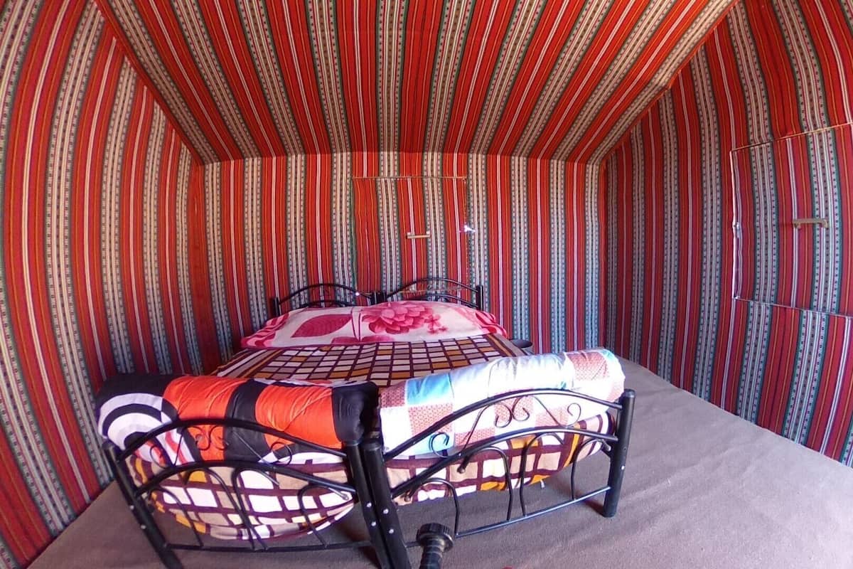 A bed with a metal frame, a patterned bedspread, and striped curtains in a room with a sloped ceiling.