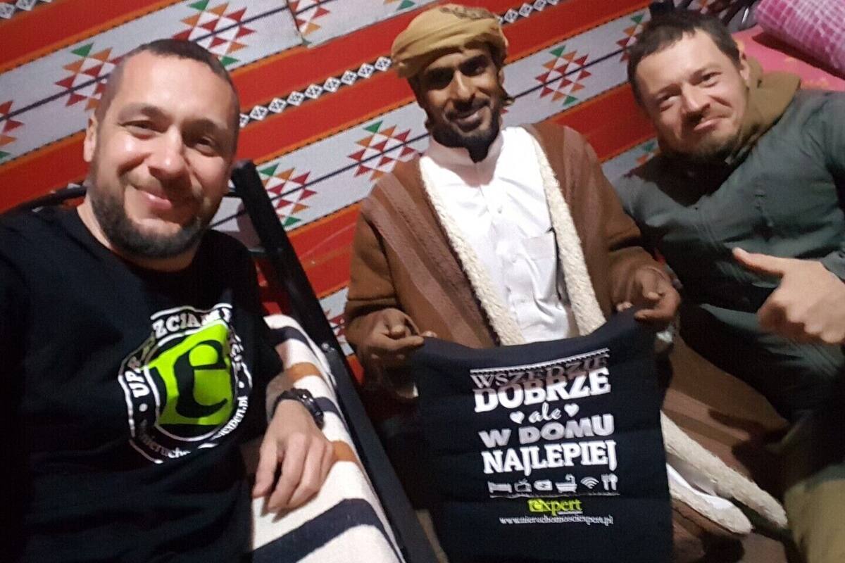 Three people sitting on a bed with a patterned blanket.
