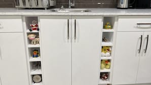 Una cocina con armarios blancos, encimera de mármol y hervidor de acero inoxidable.