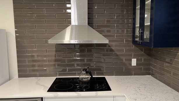 Una cocina con campana extractora de acero inoxidable, placa de inducción negra y encimera blanca.