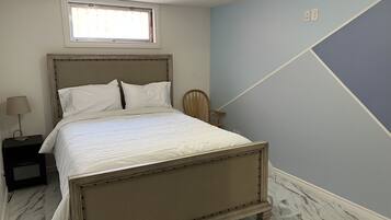 Een slaapkamer met een bed, nachtkastje, lamp, houten stoel en een raam.