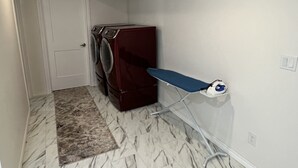 Un área de lavandería con lavadora, tabla de planchar y alfombra.
