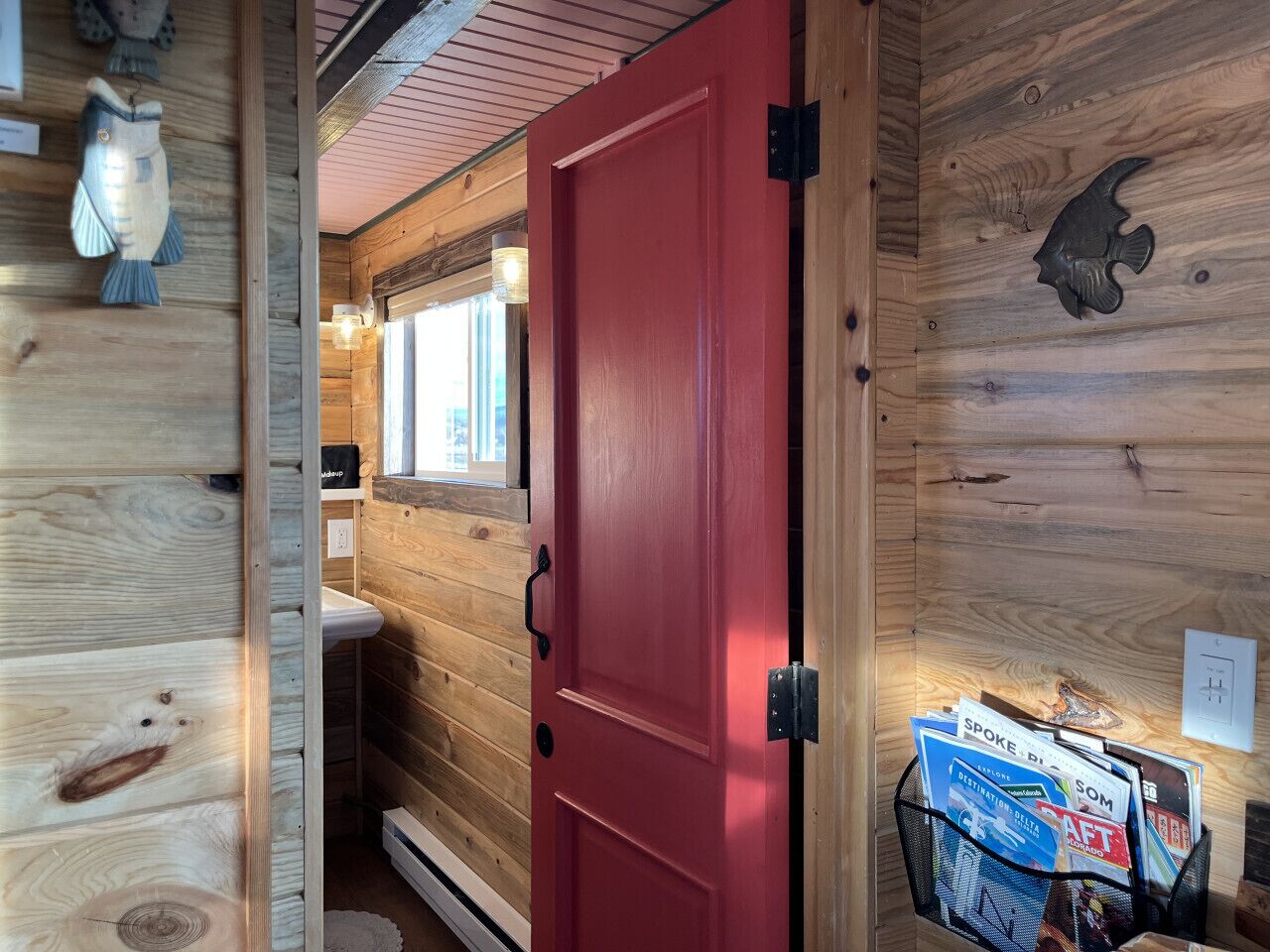 Ein Holzblockhaus-Innenraum mit einer roten Tür, einem kleinen Waschbecken und einer an der Wand befestigten Fischdekoration.
