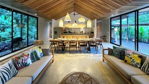 Un intérieur moderne avec un plafond en bois, un coin repas et de grandes fenêtres donnant sur un paysage verdoyant.