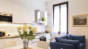 A modern kitchen with white cabinets, a dining table with chairs, and a blue sofa. - notaMI - BICOCCA Home - 2 Bedrooms (Milan)