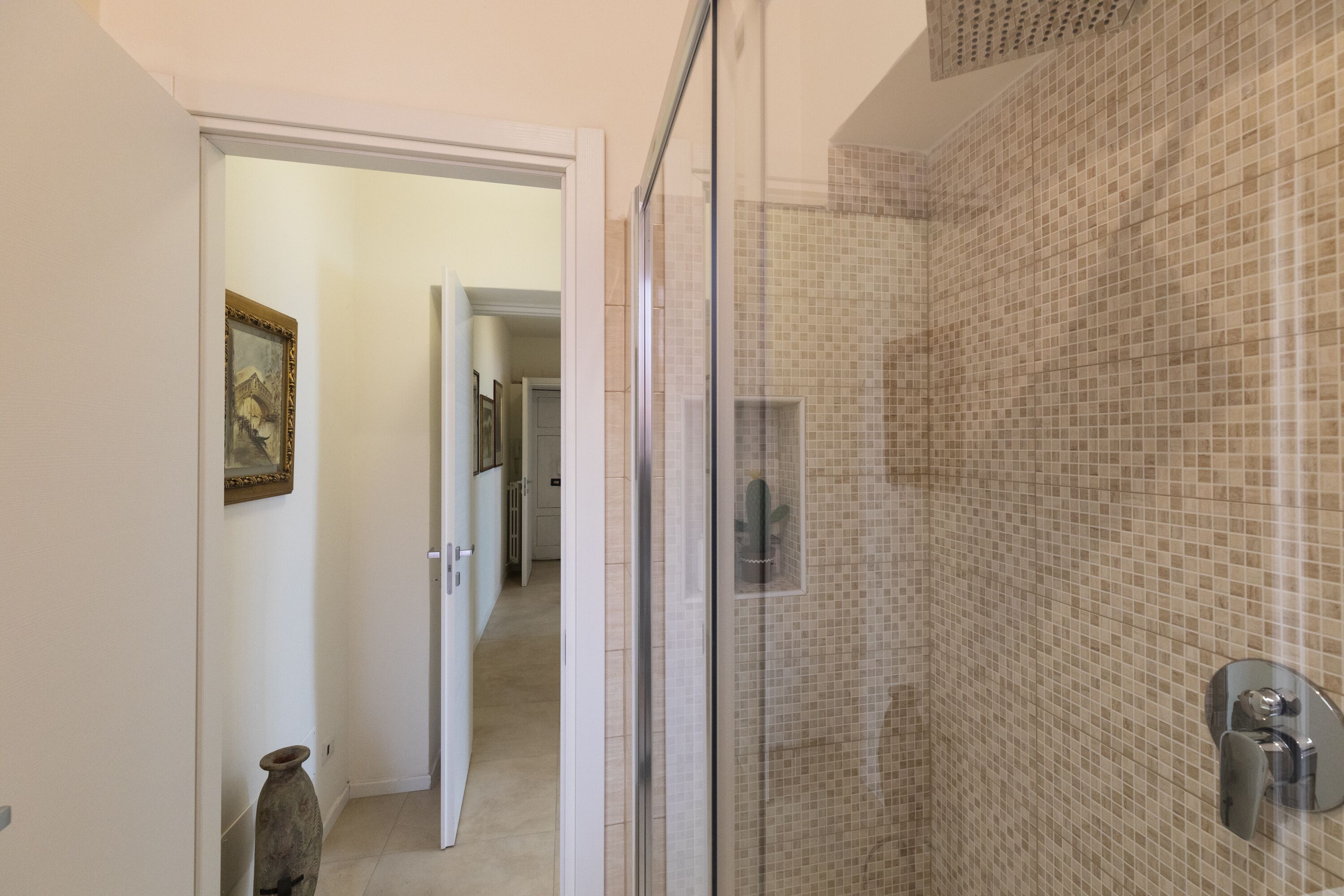 A shower with mosaic tiles, a glass door, and a visible shower control.